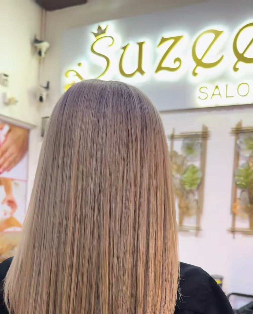 Rambut panjang lurus warna ash brown, dilihat dari belakang, di hadapan papan tanda Suzee Salon yang bercahaya